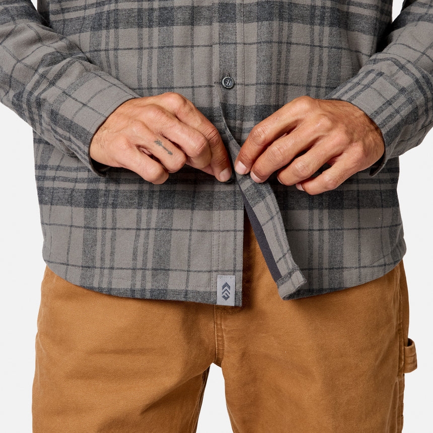 [Model is wearing size M.] A close-up of a person wearing a gray and black plaid button-up shirt, adjusting the front placket with both hands, paired with tan pants against a clean white background.