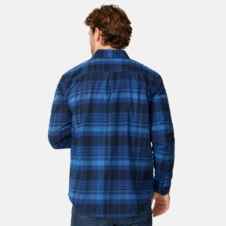 A man with short brown hair, seen from behind, wears the Free Country Men's Easywear II Fleece Lined Flannel Shirt in blue and black plaid with jeans against a plain white background.