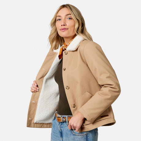 [Model is wearing size S.] A woman wearing a tan shearling-lined jacket with brown buttons, styled over a dark top and blue jeans, photographed against a clean white studio background.