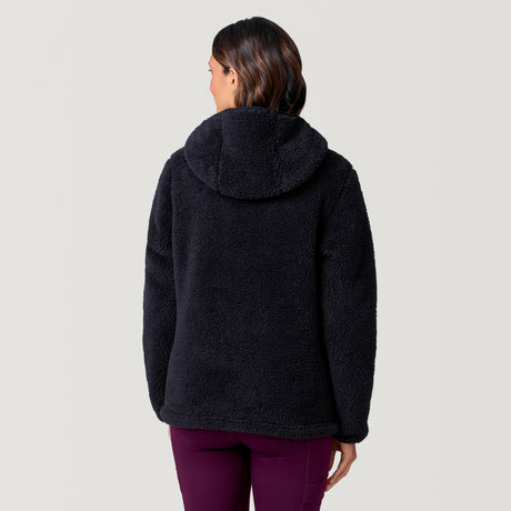 A woman is seen from behind wearing the Clearance Women's Sierra Butter Pile® Pullover Jacket in black with burgundy pants, standing against a plain light gray background.