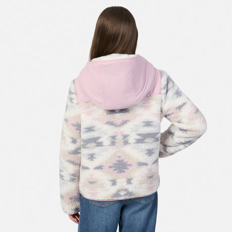 A person shown from the back wearing a fuzzy hooded jacket with a pink hood and a pale multicolor geometric pattern, paired with blue jeans, against a light gray studio background.