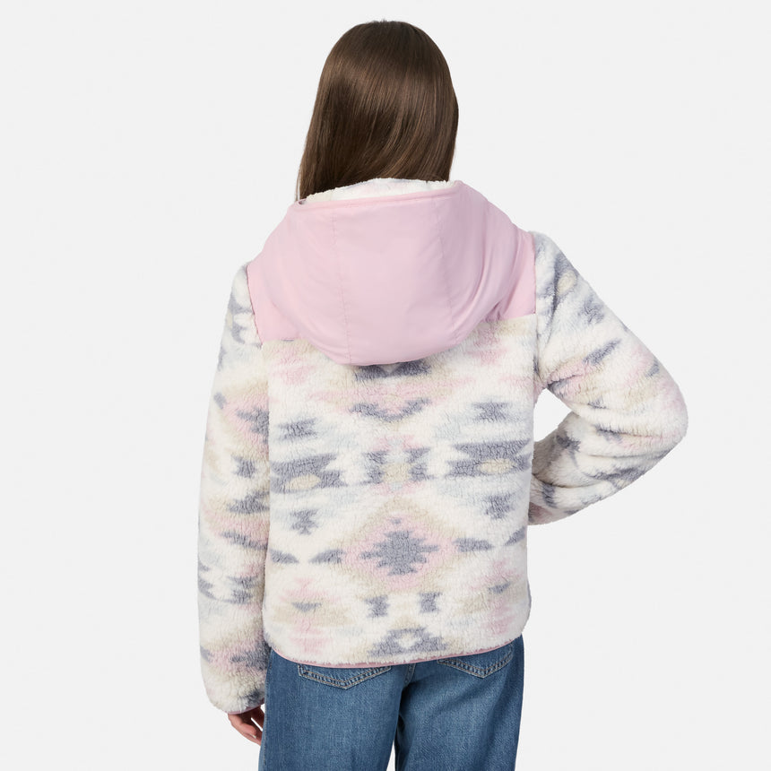 A person shown from the back wearing a fuzzy hooded jacket with a pink hood and a pale multicolor geometric pattern, paired with blue jeans, against a light gray studio background.