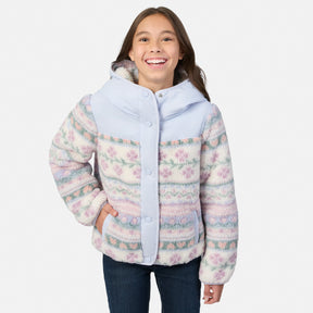 A smiling young girl wearing a hooded fleece jacket with a pastel multicolor floral pattern and light blue trim, paired with dark blue jeans, against a plain light gray background.