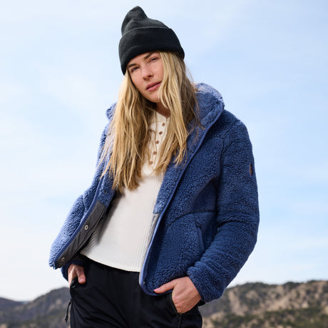 Person wearing a blue jacket and black beanie with mountains in the background
