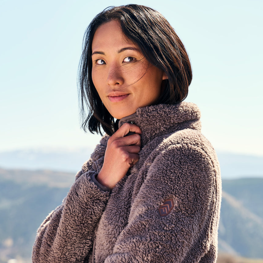 Woman wearing a brown fleece jacket with a blurred natural background
