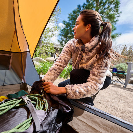 Woman in a printed sherpa fleece organizing gear beside a tent