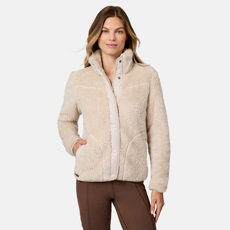 [Model is wearing size S.] A woman modeling a beige sherpa fleece jacket with a button-front placket and stand-up collar, paired with brown pants, against a light gray studio background.
