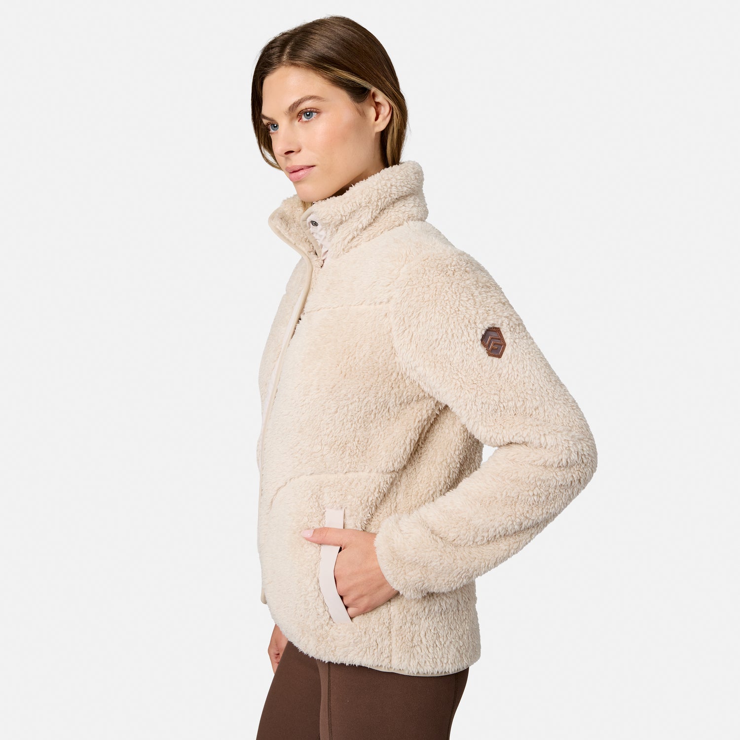 [Model is wearing size S.] A woman wearing a cream-colored sherpa fleece quarter-zip jacket with a high collar and a small brown logo patch on the upper sleeve, shown from a side profile against a light gray background.