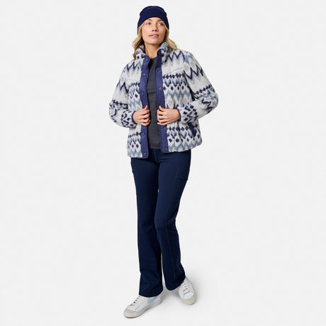 [Model is wearing size S.] A woman modeling a patterned zip-up fleece jacket, navy pants, a navy beanie, and white sneakers against a light gray studio background.