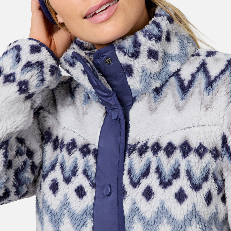 Close-up of a person wearing a fuzzy fleece jacket with a blue and white geometric pattern and a navy blue front placket.