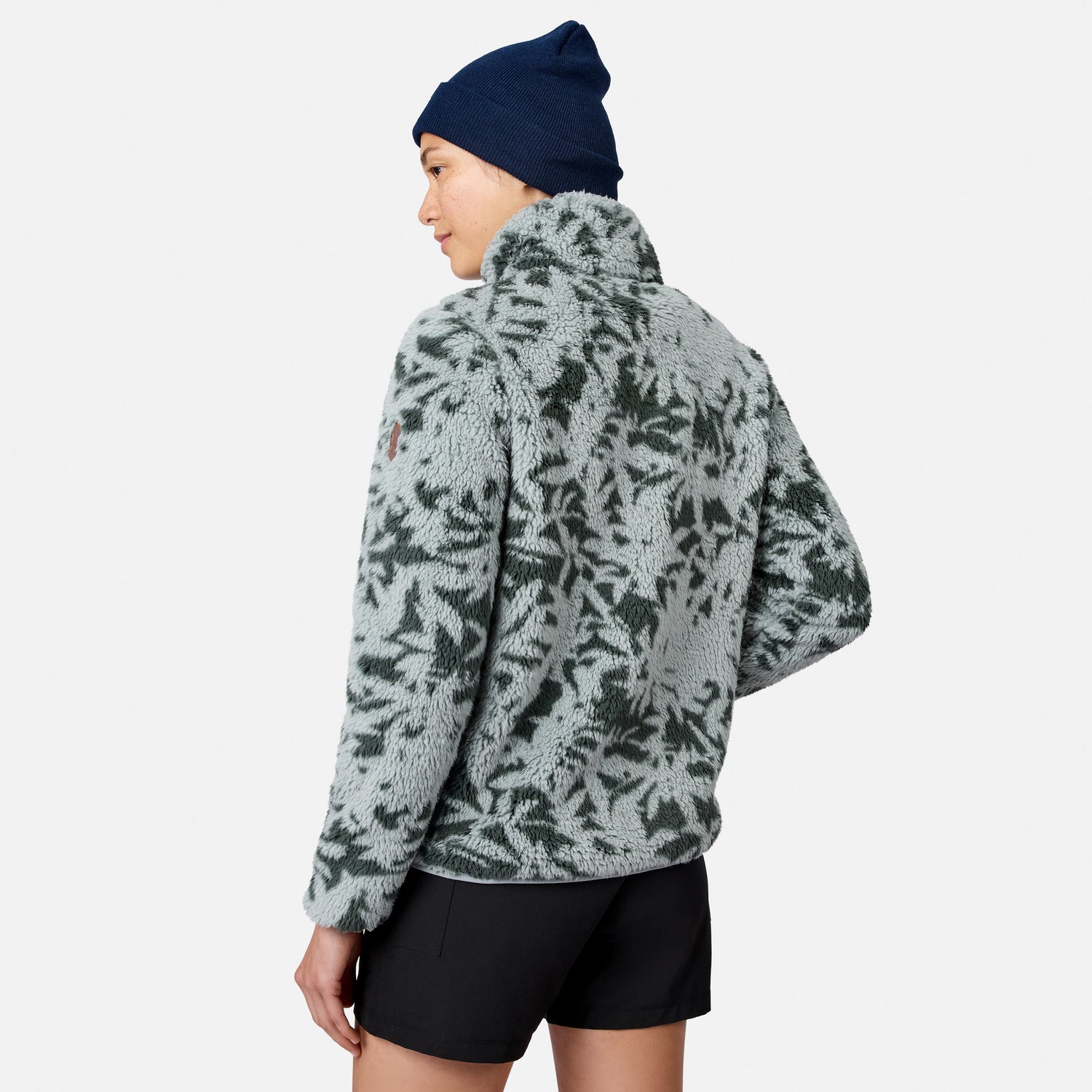 [Model is wearing size S.] A woman shown from the back wearing a light gray and dark green patterned fleece jacket, a navy blue beanie, and black shorts against a light gray studio background.