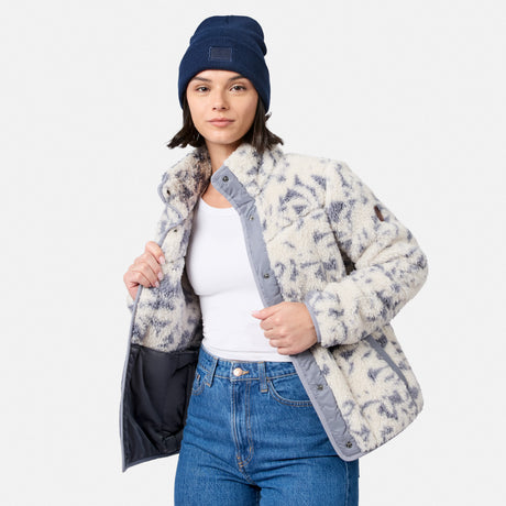 [Model is wearing size S.] A woman wearing a fuzzy sherpa-style jacket with a gray and off-white abstract pattern, a navy beanie, a white tank top, and blue jeans, photographed against a light gray studio background.