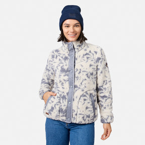 [Model is wearing size S.] A woman wearing a cream and slate blue tie-dye sherpa fleece jacket, blue jeans, and a navy blue beanie, standing against a light gray studio background.