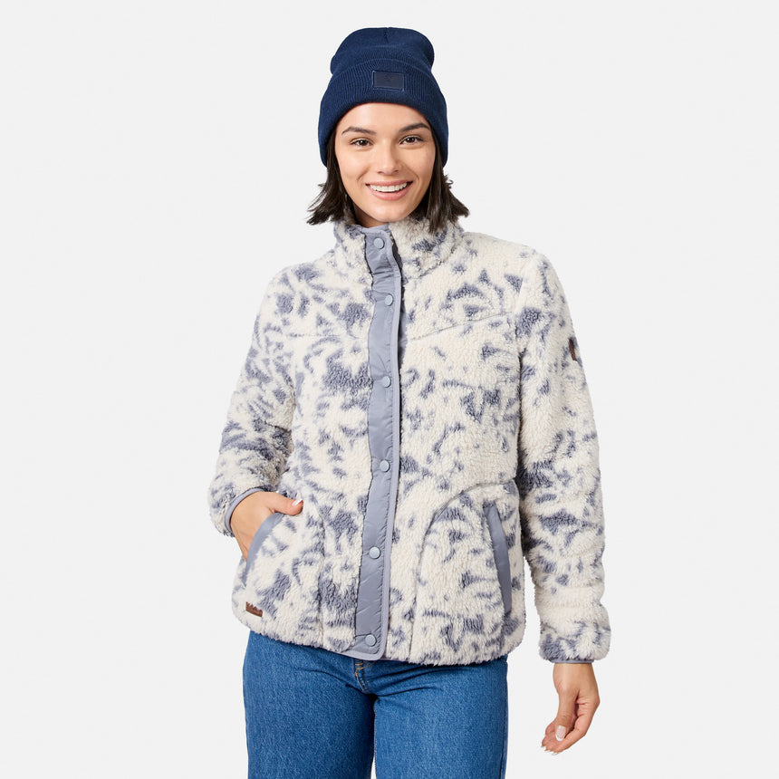 [Model is wearing size S.] A woman wearing a cream and slate blue tie-dye sherpa fleece jacket, blue jeans, and a navy blue beanie, standing against a light gray studio background.
