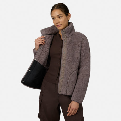 [Model is wearing size S.] A woman modeling a taupe brown sherpa fleece jacket with a high collar and snap-button front, styled over a dark brown top and pants against a light gray studio background.