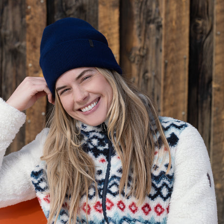 Woman wearing a blue beanie and patterned sweater against a wooden background