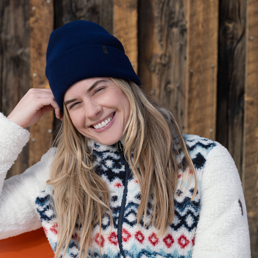 Woman wearing a blue beanie and patterned sweater against a wooden background