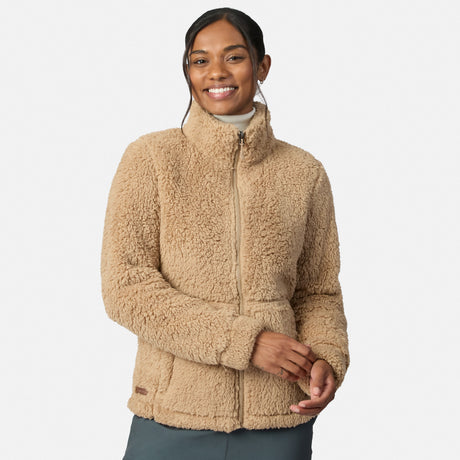 A woman smiles while wearing the Free Country Women’s Sierra Butter Pile® Zip Up Jacket in Almond and dark gray pants, standing against a plain white background.