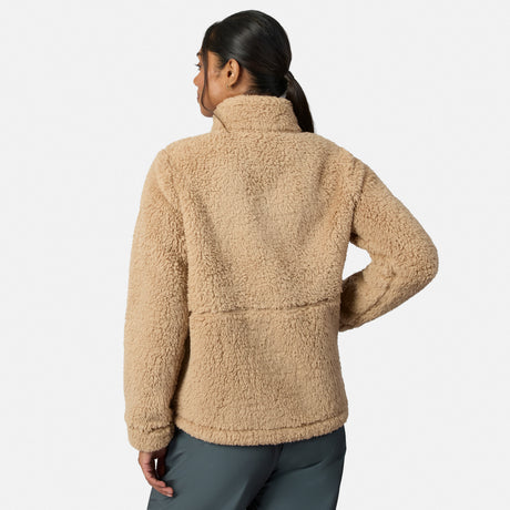 A person with long dark hair in a ponytail wears gray pants and the Free Country Women’s Sierra Butter Pile® Zip Up Jacket, standing with their back to the camera against a plain white background. The tan jacket adds cozy texture.