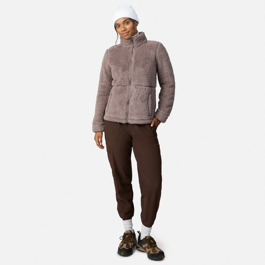 A person models the Free Country Women’s Sierra Butter Pile® Zip Up Jacket in mauve with a white beanie, dark brown joggers, white socks, and brown hiking shoes against a plain white background.