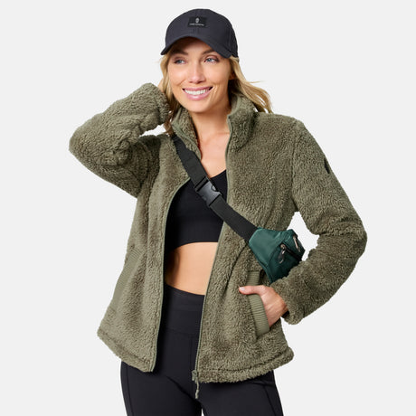 Front view of a woman wearing the olive Women's Sierra Sherpa Pile Zip Up Jacket with a crossbody bag
