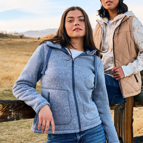 Two women standing outdoors in a field wearing jackets.