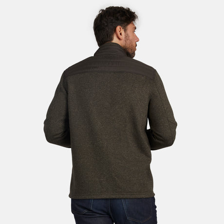 A man faces away from the camera, wearing the Free Country Men's Frore Knit Fleece Jacket in dark green with dark brown shoulder panels and a convertible collar, paired with dark blue jeans, against a plain white background.