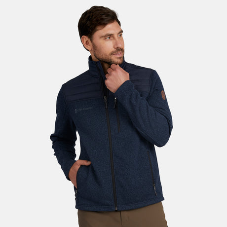 A man with short brown hair and a beard wears the Free Country Men's Frore Knit Fleece Jacket in navy blue, standing with his hand in the pocket and looking to the side against a plain light background.
