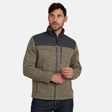 A man wearing the Free Country Men’s Frore Knit Fleece Jacket, featuring a gray and olive colorway, convertible collar, dark shoulder panels, and zippered pockets, poses with hands clasped against a plain white background.