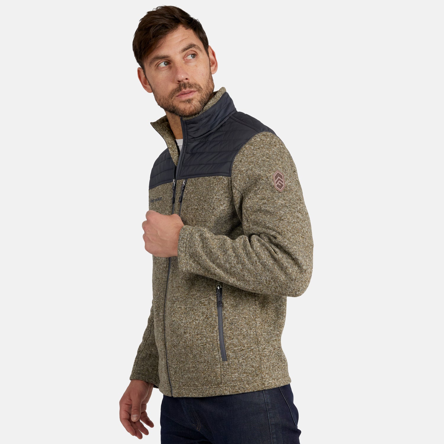 A man models the Free Country Men’s Frore Knit Fleece Jacket, showcasing its zip-up design with gray shoulders, a textured olive body, zippered pockets, and a convertible collar, as he looks over his left shoulder against a plain background.