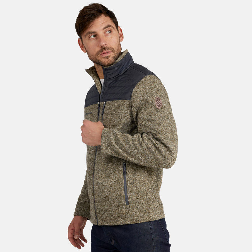 A man models the Free Country Men’s Frore Knit Fleece Jacket, showcasing its zip-up design with gray shoulders, a textured olive body, zippered pockets, and a convertible collar, as he looks over his left shoulder against a plain background.
