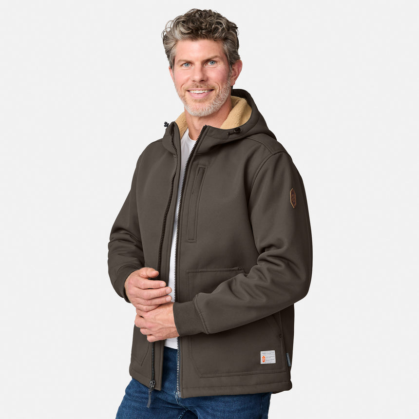 [Kolby is 6'2" wearing size M.] Men’s Free Country brown hooded jacket featuring full front zipper, two side pockets, and zippered chest pocket. Includes utility patch on left sleeve and subtle brand label at lower hem. Styled with blue jeans for a laid-back cold-weather look highlighting functional design and casual edge.
