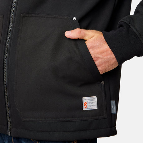 [Kolby is 6'2" wearing size M.] Men’s Free Country black hooded jacket featuring full front zipper, two side pockets, and zippered chest pocket. Includes utility patch on left sleeve and subtle brand label at lower hem. Styled with blue jeans for a laid-back cold-weather look highlighting functional design and casual edge.