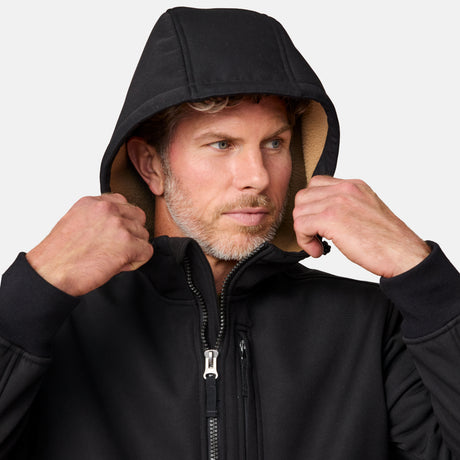 [Kolby is 6'2" wearing size M.] Men’s Free Country black hooded jacket featuring full front zipper, two side pockets, and zippered chest pocket. Includes utility patch on left sleeve and subtle brand label at lower hem. Styled with blue jeans for a laid-back cold-weather look highlighting functional design and casual edge.