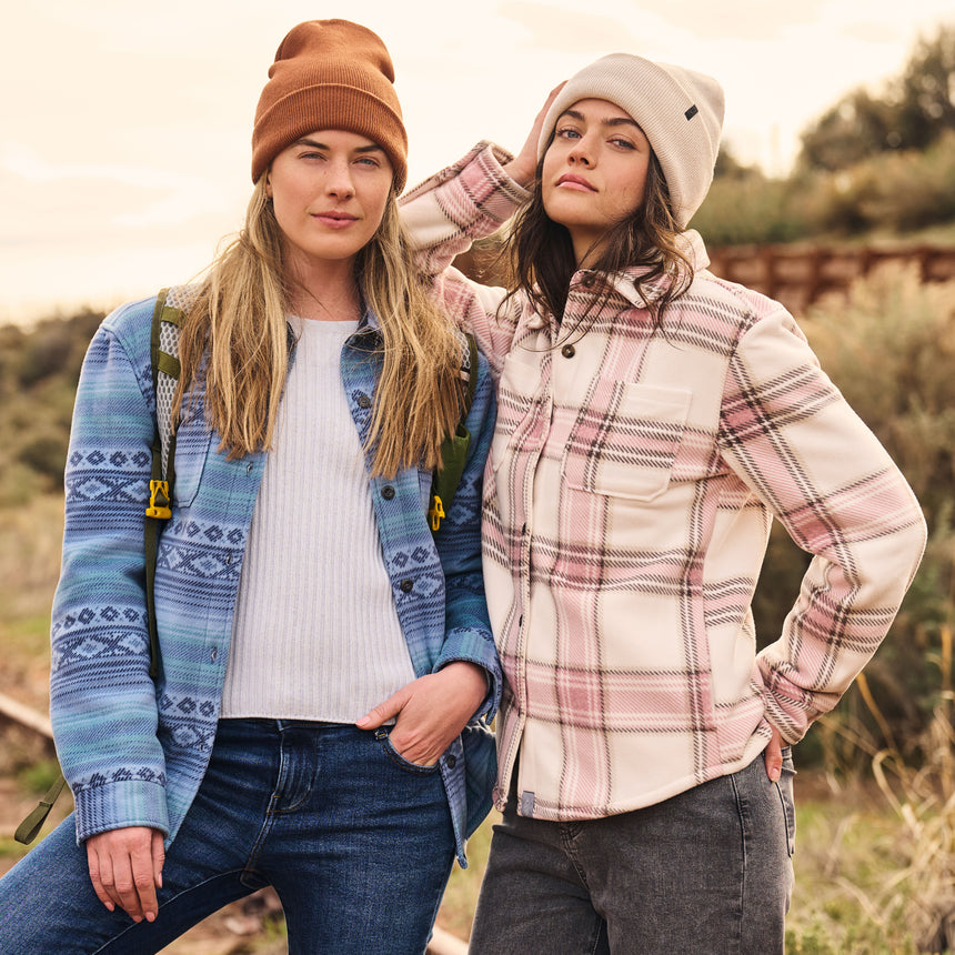 Two people standing outdoors wearing patterned jackets and beanies.