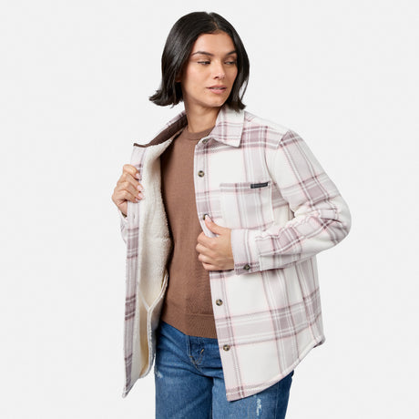 [Model is wearing size S.] A woman modeling a long-sleeve plaid overshirt with a cream sherpa lining, worn over a brown top and blue jeans against a light gray studio background.