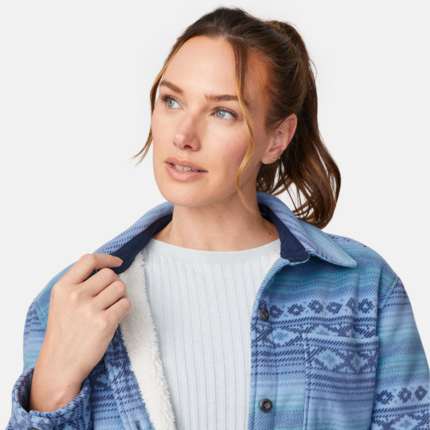[Model is wearing size S.] Close up of a woman wearing a blue patterned button-up shirt jacket over a white ribbed top and black jeans, photographed against a light gray studio background.