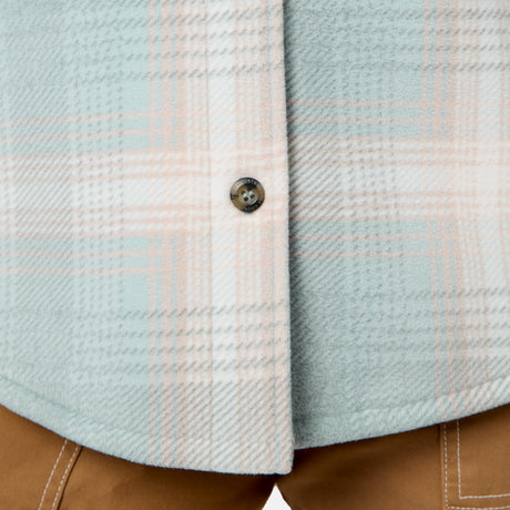 [Model is wearing size S.] Close-up of a textured plaid button-up shirt in light blue, white, and pale pink, with a brown button, worn over tan pants.