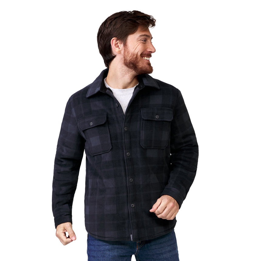 A smiling man wears a Free Country Men’s Chill Out Fleece Shirt Jacket in dark plaid over a white t-shirt and blue jeans.