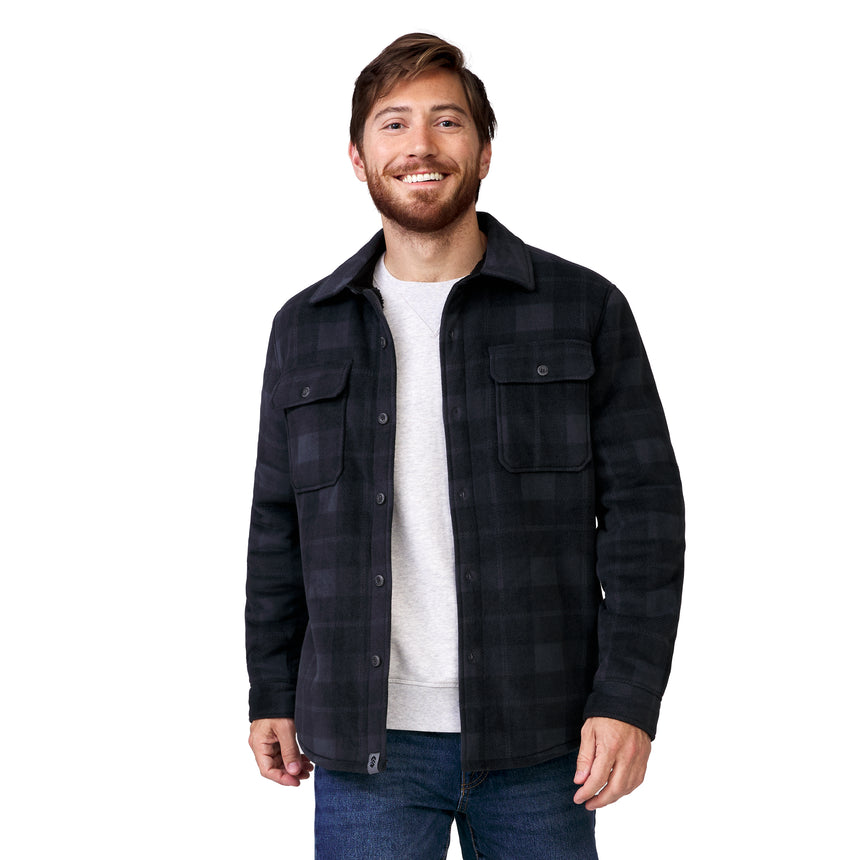 A smiling man wearing a dark gray plaid Free Country Men’s Chill Out Fleece Shirt Jacket over a light gray crew-neck shirt and blue jeans.