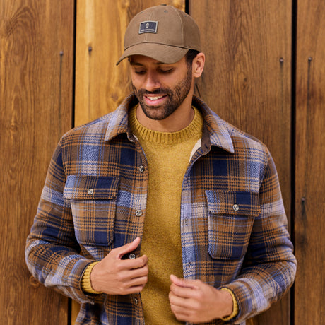 Man wearing a plaid shirt and brown cap against a wooden background