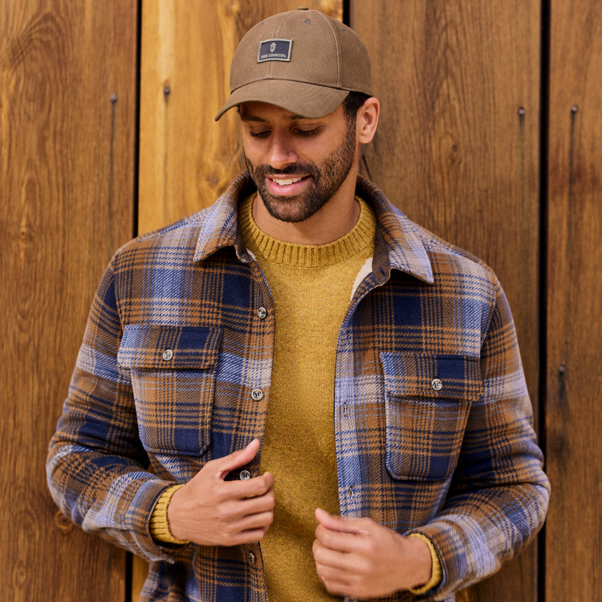 Man wearing a plaid shirt and brown cap against a wooden background