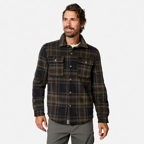 A man with dark hair and a beard wears the Free Country Men’s Chill Out Fleece Shirt Jacket in Olive Plaid, featuring chest pockets, as he stands and smiles against a plain white background.