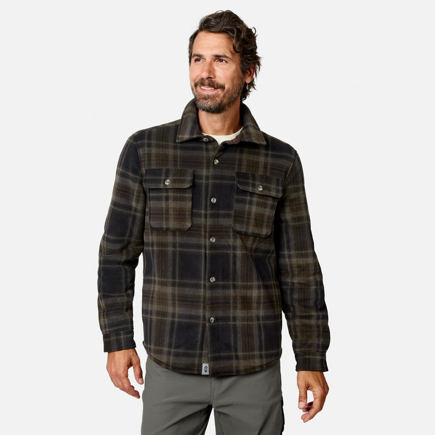 A man with dark hair and a beard wears the Free Country Men’s Chill Out Fleece Shirt Jacket in Olive Plaid, featuring chest pockets, as he stands and smiles against a plain white background.