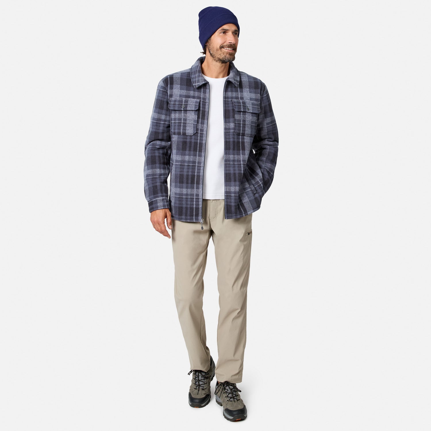 [Model is wearing size M.] A man wearing a navy and gray plaid button-up shirt jacket over a white t-shirt, khaki pants, and a navy beanie, standing against a light gray studio background.