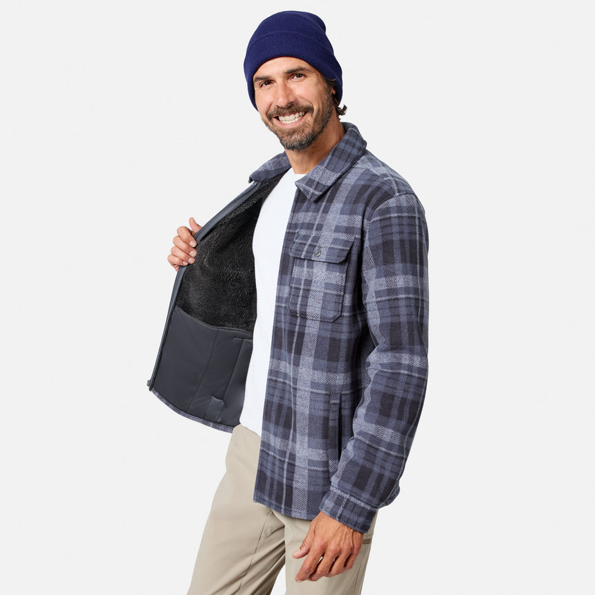 [Model is wearing size M.] A man wearing a navy blue beanie, a gray and blue plaid flannel shirt with a dark fleece lining, and beige pants, holding open the shirt to show the interior lining against a light gray background.