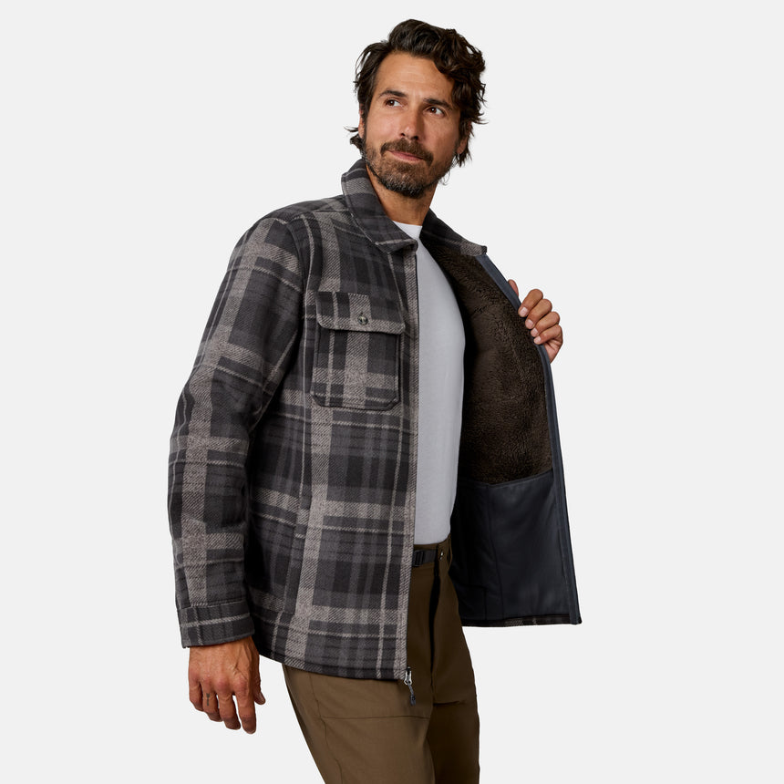 [Model is wearing size M.]A man wearing a dark gray and black plaid overshirt jacket with a brown sherpa lining, shown against a light gray studio background.