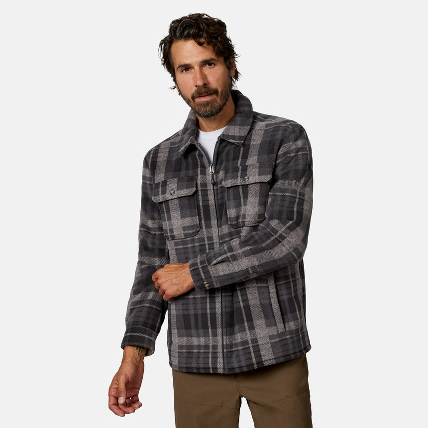 [Model is wearing size M.]A man wearing a dark gray and black plaid overshirt jacket with a brown sherpa lining, shown against a light gray studio background.
