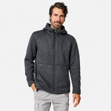 [Model is wearing size M.] A man with wavy brown hair and a beard wears a Men’s Mountain Fleece Jacket by Free Country in Black Texture, known for its lightweight warmth, paired with light gray cargo pants. He stands against a plain white background, with one hand in his pocket.