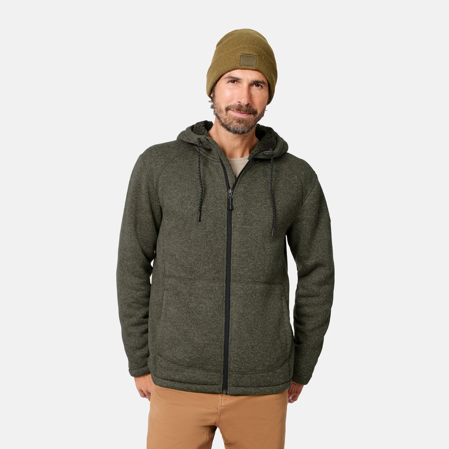 [Model is wearing size M.] A man wearing a mushroom-colored Men’s Mountain Fleece Jacket by Free Country, paired with tan pants and an olive beanie, stands against a plain white background, looking at the camera with a slight smile. This lightweight sweater fleece jacket provides warmth and effortless comfort for everyday wear.